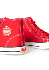Sneakers alti rossi in tela, con cuciture bianche, un'etichetta rotonda e una striscia nera lungo la suola in gomma.