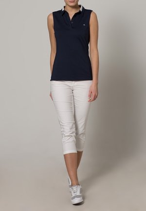Navy sleeveless polo with a collar and white trim, paired with white cropped pants and gray sneakers. Smooth, breathable fabric.