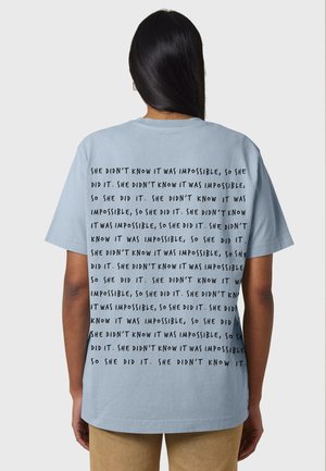 T-shirt en coton bleu clair à manches courtes et col rond, avec du texte noir répété au dos dans une police en gras.
