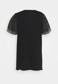 Robe noire longueur genou avec manches bouffantes transparentes et décolleté rond, vue de dos sur fond blanc.