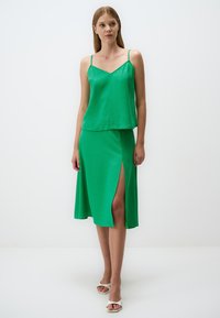 Ensemble vert en deux pièces comprenant un haut sans manches avec un décolleté en V et une jupe de mi-longueur avec une fente sur le côté. Fabriqué dans un tissu lisse et léger.