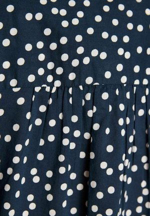 Mørkeblåt stof med hvidt polkaprikket mønster og sammensyet detalje, der skaber bløde folder.