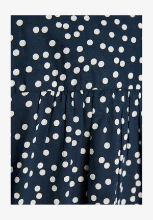 Mørkeblåt stof med hvidt polkaprikket mønster og sammensyet detalje, der skaber bløde folder.