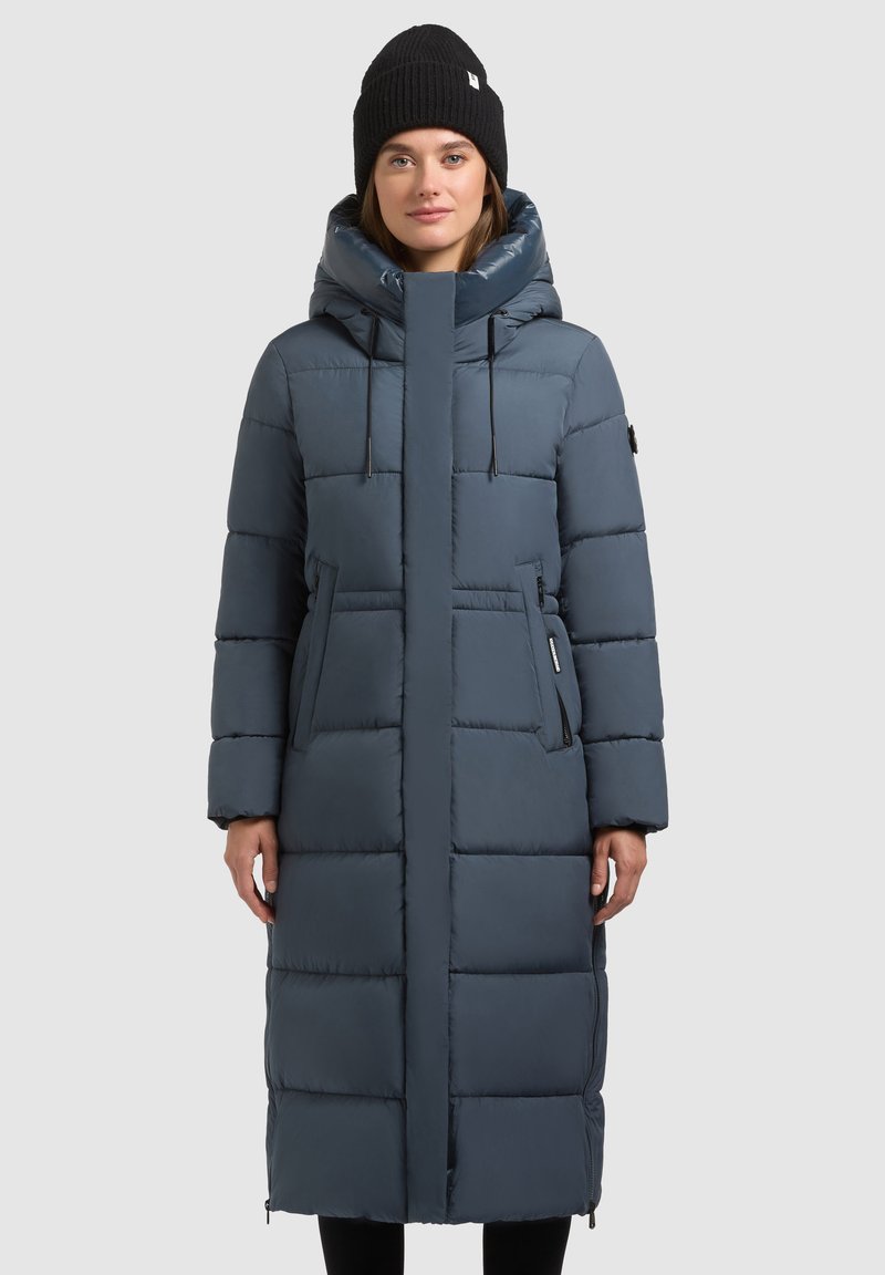 Lang, fyldig jakke i mørkeblå med høj krave, snørejusterbar hætte og sidelommer; har en glat, blank finish og vandrette søm.