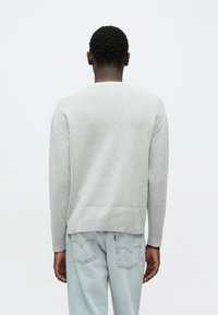 Pull-over gris clair en tissu doux avec ourlet et poignets côtelés, associé à un jean en denim bleu clair avec poches arrière.