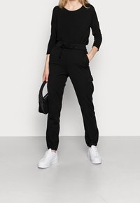 Zwarte lange mouwen top gecombineerd met zwarte joggerbroeken met zijzakken, een strik taille en elastische boorden, aangevuld met witte sneakers.