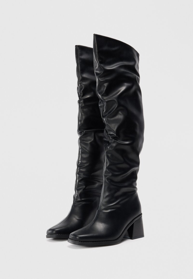 Bottes noires montantes en cuir lisse, avec un design flou, un bout pointu et un talon épais pour la stabilité et le style.