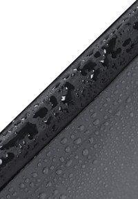 Superficie negra con gotas de agua. El material parece suave con un acabado mate. La textura varía con pequeñas y distintas perlas de agua.