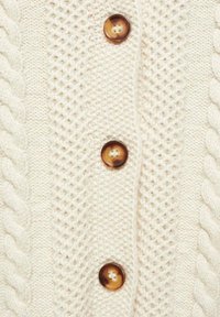 Cremefarbener Cardigan mit einem strukturierten Strickmuster und Zopfmusterdetails, sowie vier braunen Knöpfen auf der Vorderseite.