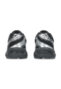Chaussures de sport noires avec des accents argentés, dotées d'une tige en maille, d'un col rembourré et d'une semelle en caoutchouc texturée pour une meilleure adhérence.