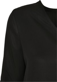 Svart bluse med V-hals, lange ermer og glatt, lett glinsende tekstur. Enkelt design uten synlige mønstre eller detaljer.