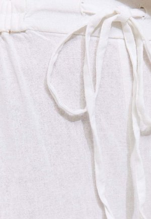 Gros plan sur un tissu en lin blanc doux avec un cordon de serrage noué à la taille, mettant en valeur la texture et la légèreté du matériau.