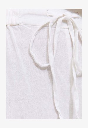 Gros plan sur un tissu en lin blanc doux avec un cordon de serrage noué à la taille, mettant en valeur la texture et la légèreté du matériau.