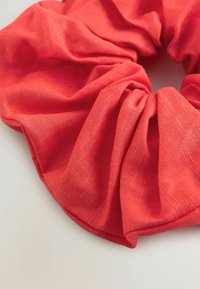 Punane kangast scrunchie, mis on valmistatud tekstuuritud materjalist, millel on kogutud disain ja siledad servad, ideaalne juuste kinnitamiseks.