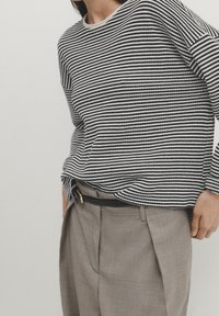 Maglione a righe bianche e nere con colletto rotondo, abbinato a pantaloni plissettati marrone chiaro e una cintura nera. Tessuto texture.