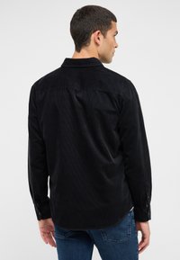 Schwarzes Cord-Hemd mit einem Button-Down-Kragen, langen Ärmeln und einer strukturierten Stoffoberfläche. Verfügt über einen abgerundeten Saum und mit Knöpfen verschließbare Manschetten.