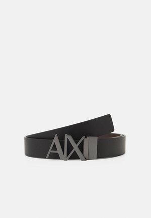 Ceinture en cuir noir roulée avec une boucle en métal noir présentant les lettres stylisées A, X et I sur un fond clair uni.