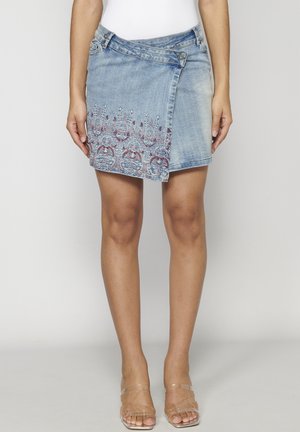 Jupe en denim mini avec un design asymétrique, délavage bleu clair et broderies florales décoratives en rouge et bleu au niveau de l'ourlet.