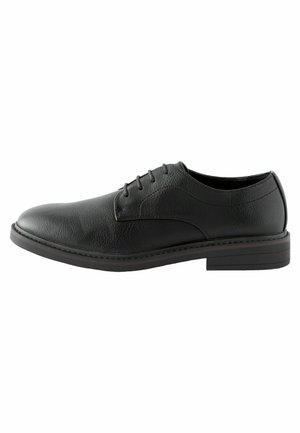 Zapato negro de cuero con cordones, de textura suave, punta redondeada y suela plana de goma. Presenta costuras sutiles a lo largo del borde.
