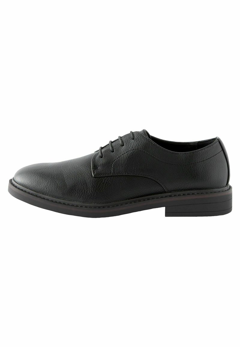 Zapato negro de cuero con cordones, de textura suave, punta redondeada y suela plana de goma. Presenta costuras sutiles a lo largo del borde.