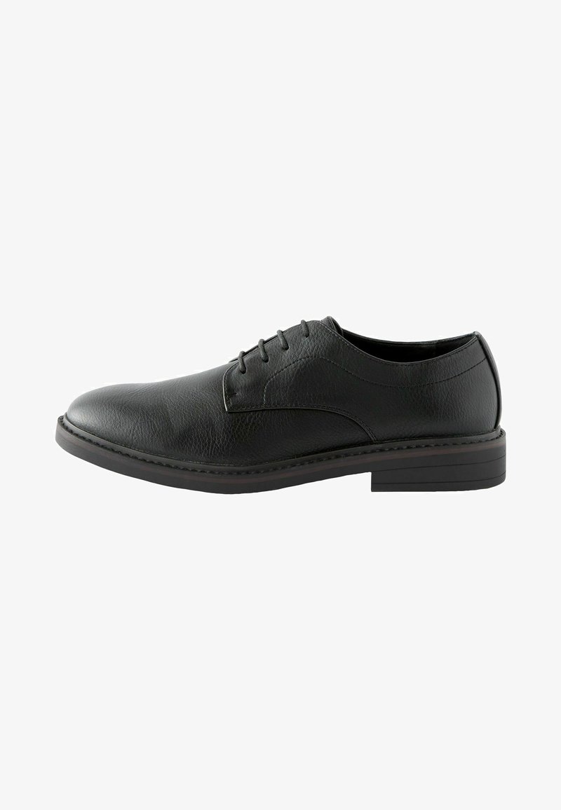 Zapato negro de cuero con cordones, de textura suave, punta redondeada y suela plana de goma. Presenta costuras sutiles a lo largo del borde.