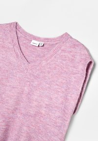 Svetřík bez rukávů s výstřihem do V, v měkké, texturované světle růžové barvě s jemným melírovaným vzorem. Na límci jsou viditelné cedulky.