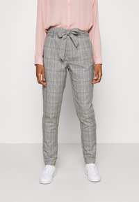 Grå rutiga byxor med papperpåse midja och ett knytbälte, kombinerat med en ljusrosa långärmad skjorta och vita sneakers.