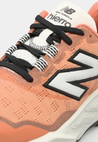 Baskets corail et blanches avec un upper en maille texturée, des lacets et des accents noirs, un logo 'N' blanc prominent, et une semelle rembourrée.