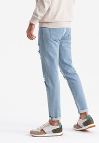 Jasnoniebieskie zniszczone dżinsy o luźnym kroju, z podwiniętymi nogawkami i postrzępionymi detalami, w połączeniu z wielokolorowymi casualowymi sneakersami.