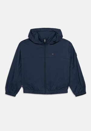 Veste à capuche bleu marine avec fermeture éclair frontale, poignets et ourlet élastiques, deux poches latérales, et petit logo rouge, blanc et bleu sur la poitrine.
