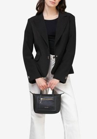 Sort skræddersyet blazer med skarpe revers, parret med en sort håndtaske med lynlås-lomme og dobbelte hanke. Hvide bukser fuldender outfittet.