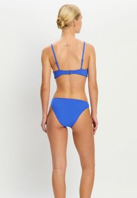 Bikini bleu en tissu lisse. Dispose de fines bretelles réglables et d'un fermoir à l'arrière. Bas taille haute avec une couverture minimale.
