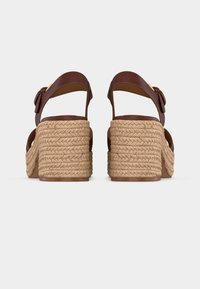 Paire de sandales en cuir marron avec talons compensés en corde tressée vues de dos sur fond blanc.