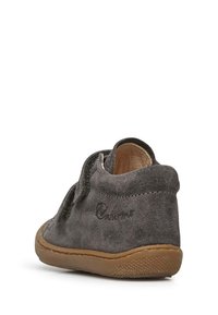 Chaussure en suède gris avec une surface texturée, profil bas et semelle en caoutchouc marron. Elle est équipée d'une sangle Velcro pour un maintien facile.