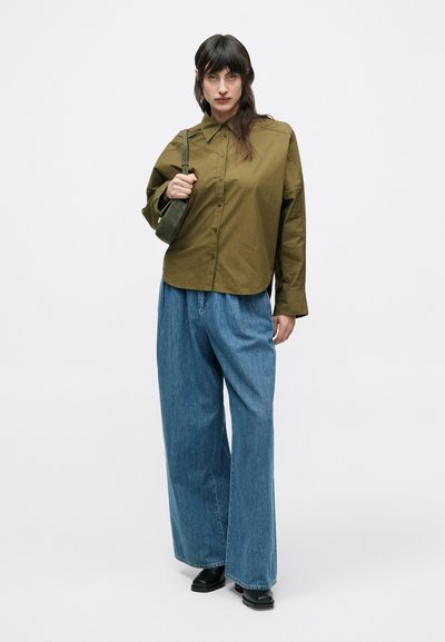 Πράσινο πουκάμισο με κουμπιά, άνετο τζιν σε μπλε απόχρωση και μαύρα μποτάκια μέχρι τον αστράγαλο. Απλός σχεδιασμός με γιακά και ευθύγραμμα παντελόνια.