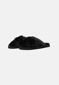 Pantofole nere in morbido pelliccia sintetica, con suola piatta, design open-toe e texture soffice. Presentano cinture larghe per il massimo comfort e una base nera liscia.