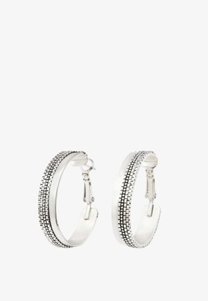 Boucles d’oreilles créoles en argent avec une bande noire à pois texturée au centre, dotées d’un fermoir à charnière sur fond blanc.