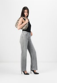 Grijze high-waisted straight-leg jeans gecombineerd met een zwarte mouwloze top en zwarte puntige hakken, terwijl ze een tas met een patroon van slangprint vasthoudt.