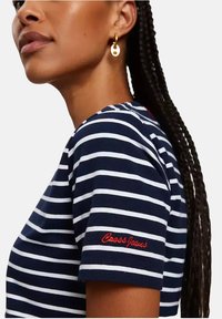 T-shirt w paski w kolorze granatowym i białym z krótkimi rękawami, z czerwonym haftowanym napisem "Cross Jeans" na rękawie. Gładka bawełniana tekstura.