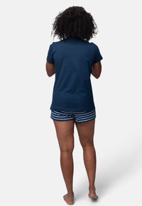 Camicia navy a maniche corte abbinata a pantaloni corti a righe. I pantaloni corti presentano righe bianche orizzontali. Il tessuto appare morbido e informale.