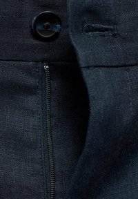 Gros plan sur un tissu foncé avec un bouton noir, une boutonnière et une fermeture éclair verticale visible sur un vêtement.