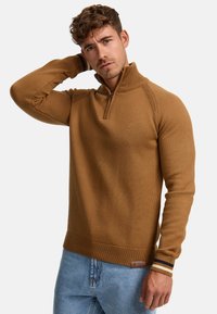 Bruine gebreide sweater met een kwart-rits kraag, geribde manchetten en zoom, voorzien van een klein logo op de borst en contrasterende gestreepte accenten.