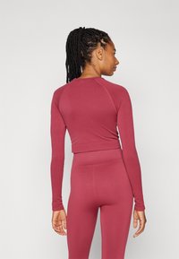 Burgundi színű, hosszú ujjú, cropped top sima anyagból, bordázott részletekkel. Testhez simuló fazon, kerek nyakkivágással és kifinomult sziluettel.