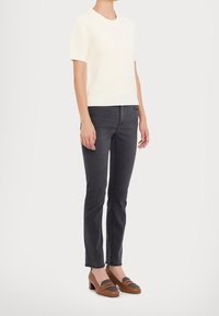 Pull à manches courtes en maille côtelée crème, associé à un jean gris foncé slim et des mocassins marron à talons avec des accents gris. Design simple et moderne.