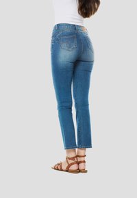 Blauwe spijkerbroek met een mid-rise taille, achterzakken met stikseldetails en een cropped pasvorm, gecombineerd met bruine sandalen met bandjes.