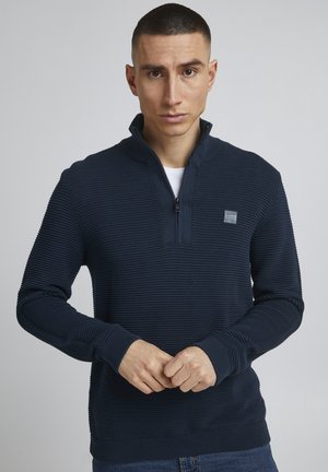 Mornarska zip-up dukserica ima teksturirani rebrasti dizajn, visoki ovratnik i elastične rukave. Mala logotip zakrpa na lijevoj strani prsnog koša. Prilagođen kroj.