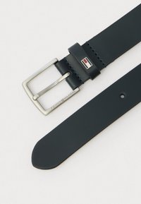 Tumed nahkrihm hõbedaste metallist klambri ja logo aktsendiga. Omab sujuvat tekstuuri ja mitmeid reguleerimisavasid suuruse kohandamiseks.