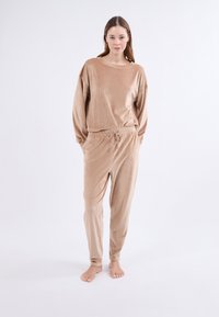 Beżowy zestaw dresowy z corduroy, składający się z luźnej bluzki z długimi rękawami oraz spodni z troczkami i zwężanymi nogawkami, wykonanych z teksturowanej tkaniny.