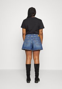 Czarny t-shirt z krótkim rękawem, niebieskie szorty dżinsowe z dwoma tylnymi kieszeniami, żółta metka, w połączeniu z czarnymi zamszowymi kozakami do kolan.