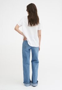 Hvid bomuldstrøje parret med lyseblå denimjeans. Jeansene har lige skæring med oppullede bomuldsmanchetter og en lomme-detail på bagenden.